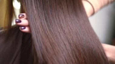 Yakın plan kadın elleri, parlak lamine esmer saçlarını yavaş çekimde gösteriyor. Beyaz tenli kuaför, kuaförde keratin laminasyon efektiyle övünüyor.