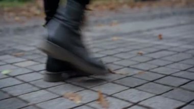 Siyah deri çizmeli genç bir kadının kaldırımda yürürken çekilen ayak izleri. Sonbahar gününde şehir caddesinde yürüyen tanınmayan bir kadın. Yaşam tarzı kavramı