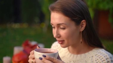 Açık havada sıcak çay içen gülümseyen genç bir kadının yakın plan portresi. Kaygısız, rahat, Kafkasyalı güzel bayan arka bahçede lezzetli içkinin tadını çıkarıyor. Huzur ve yaşam dengesi