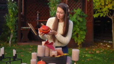 Arka bahçeyi Jack-o-Lantern ile dekore eden genç ve mutlu bir kadın ve kameraya bakan mumlar yavaş çekimde gülümsüyor. Cadılar Bayramı 'nda açık havada poz veren kendinden emin beyaz kadın portresi.
