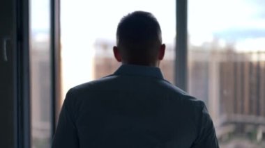 Yeni evdeki pencereye doğru yürüyen ve şehir şehrine bakan genç bir adamın arka plan silueti. Tanımlanamayan beyaz adam apartman dairesini seçiyor. İnşaat aşamasında.