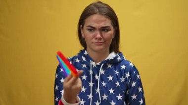 Tereddüt eden beyaz tenli esmer kadın kameraya bakıyor ve oyuncak tutuyor. Belirsiz çekici kadının portresi sarı arka planda poz veriyor popüler duyusal oyuncakla ağır çekimde