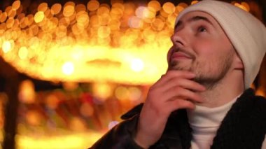 Yakın plan beyaz adam gülümsüyor ve arka planda Noel ışıklarıyla gece dışarı bakıyor. Mutlu kaygısız adam şehir merkezinde yeni yılın tadını çıkarıyor.