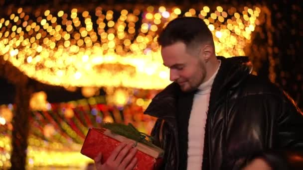 一个心满意足的快乐男人的画像 带着圣诞礼物站在城市街道的夜晚 年轻的白人帅哥在户外等待新年前夜的约会 生活方式和幸福 — 图库视频影像