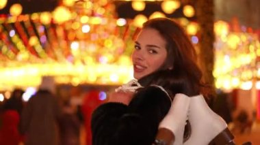 Omuzlarında buz pateniyle gülümseyen güzel bir kadının Noel gecesi şehir caddesinde yürürken kameraya bakarken çekilen görüntüsü. Mutlu Kafkas genç bayan kışın tadını çıkarıyor