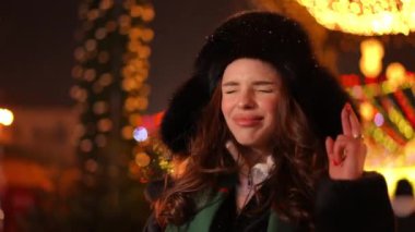 Olumlu kadın yeni yıl arifesinde gece şehrinde dua ediyor. Gülümseyen beyaz bir bayanın portresi Noel 'de en iyisini diliyor. Yaşam tarzı ve umut.