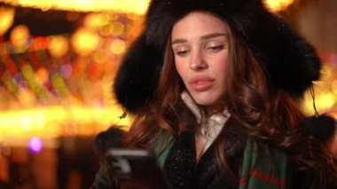 Akıllı telefon uygulamasında sosyal medyada yavaş çekimde konuşan özümsenmiş bin yıllık kadın. Kentte Noel gecesi internette sörf yapan kendine güvenen beyaz bir kadının portresi.