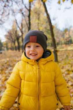 Sonbahar parkında sarı ceketli ve gülümseyen tatlı bir oğlan.
