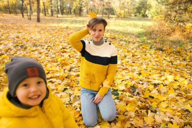 Mutlu anne ve küçük oğlu sonbahar parkında birlikte eğleniyor sarı yaprakların arasında ve gülümsüyor.