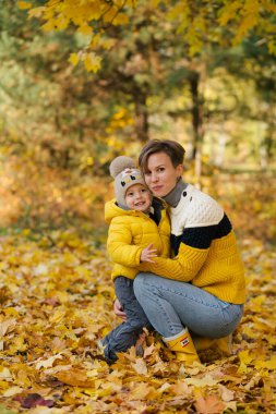 Anne ve Oğul gülerek ve gülerek sonbahar parkında sarı yaprakların arasında
