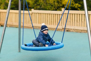 Sahada salıncakta sallanan mavi kot giysili tatlı çocuk.