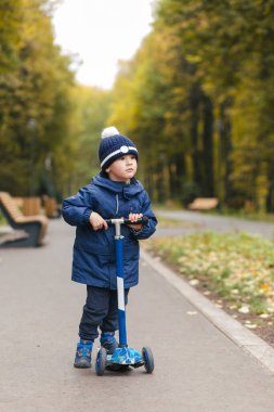 Sonbahar parkında şık bir kıyafetle motosiklete binen tatlı bir erkek bebek.