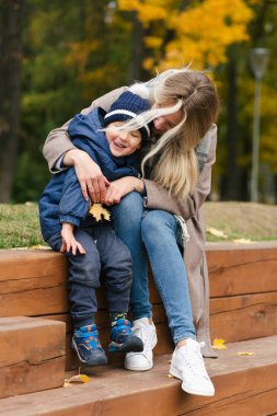 Mutlu anne oğlunu kucaklıyor tahta parkta oturuyor ve gülümsüyor.