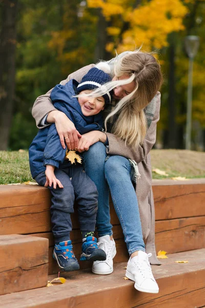 Mutlu anne oğlunu kucaklıyor tahta parkta oturuyor ve gülümsüyor.