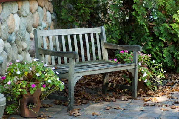 Деревянная скамейка с цветами и опавшими листьями — стоковое фото