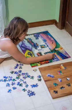 Genç bir kız, yatak odasının zemininde yapboz üzerinde çalışırken rahatlıyor.