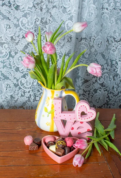 spring pink tulips are in a pretty pitcher with a lace back ground and gourmet chocolates