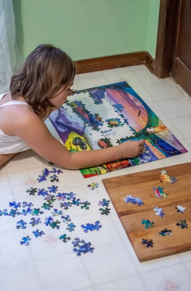 Genç bir kız, yatak odasının zemininde yapboz üzerinde çalışırken rahatlıyor.