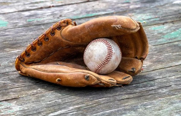 Old worn baseball glove holds an ancient, dirty baseball, a beautiful still life for a boy of any age