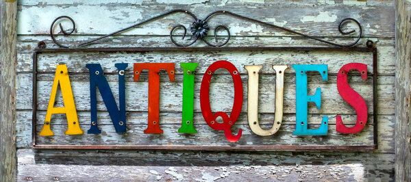красочный металлический знак, который обозначает антиквариат висит на деревенской деревянной стене в старинном сарае