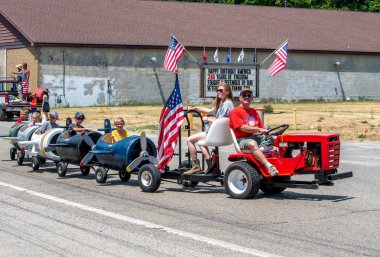Eau Claire MI USA 4 Temmuz 2022; 4 Temmuz geçit töreninde şamandıralar süslü olmak zorunda değil. Bu aile, bu bayram töreninde çocukları küçük uçaklara bindirmek için çim biçme makinesi kullanıyor.