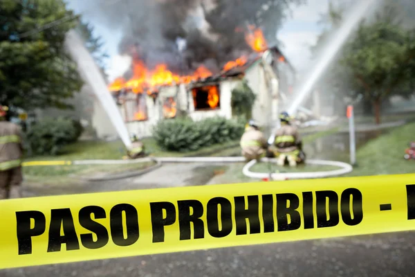 Spanish Paso Prohibido tape with firefighters and a burning hous — Stock Photo, Image