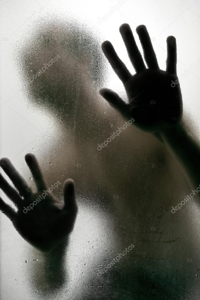 Silhouette of a man with hands on a frosted glass