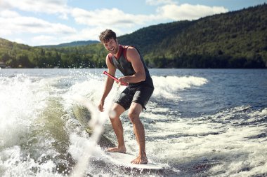 Happy handsome man wakesurfing in a lake clipart