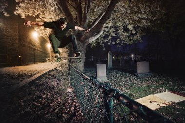 kaykaycı ollie hüner bir çitin üzerinden geceleri yapıyor.