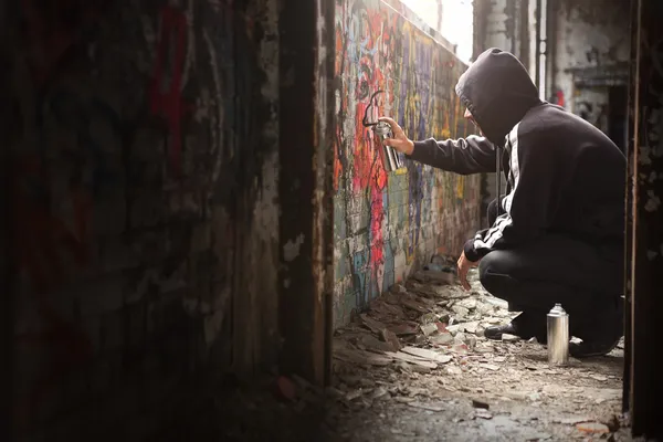 Junger Mann sprüht schwarze Farbe auf Graffiti-Wand. Stockbild