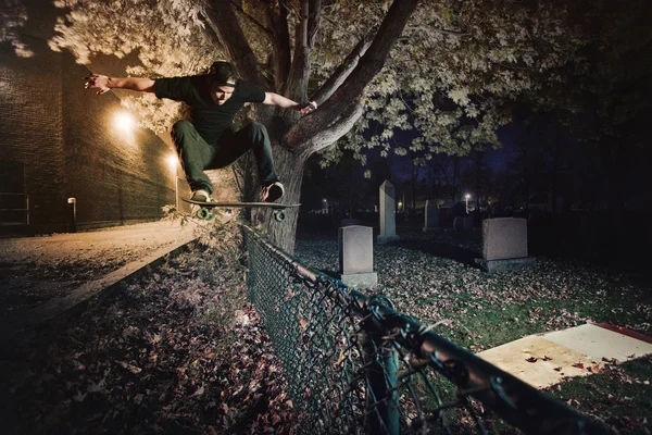 Skateboarder haciendo un truco de Ollie sobre una valla por la noche Imágenes de stock libres de derechos