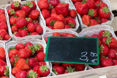 Strawberry market baskets with many delicious red strawberries. Cups of fresh sweet quality strawberries at marketplace. Local bio fruit sale with euro price tag and blank black label copyspace.