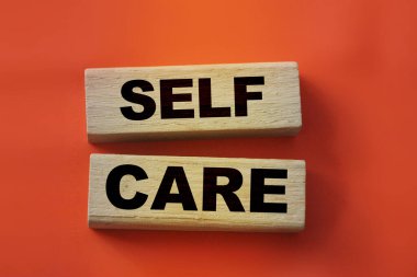 SELF CARE - kırmızı gradyan arkaplan üzerinde tahta küplerle ilgili metin.