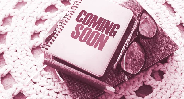 Coming soon on the cover of copybook, glasses and pen on crochet carpet. Business and education program concept.