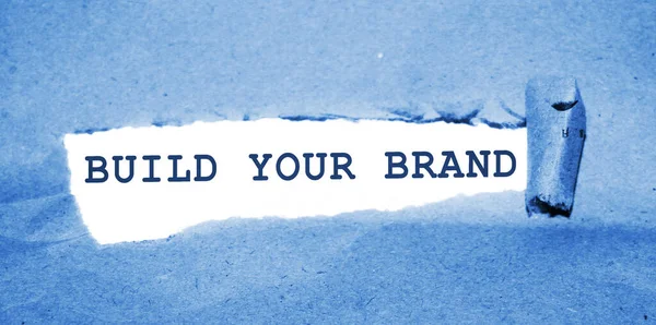 BUILD YOUR BRAND message written under torn paper. Branding rebranding marketing business concept.