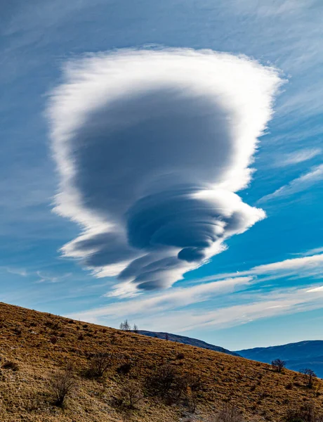 Strange shaped clouds in blue sky with sunlight above Dinaric Alps. Cloudy blue sky with white cloud in form of lenses lenticular over autumn Dinara mountains. White clouds shaped as spinal column.