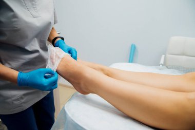 Mavi eldivenli kadın elleri müşterinin ayaklarına tek kullanımlık çoraplar giydirdi. Güzellik salonu ya da tıbbi prosedürler. Masaj veya pedikür.