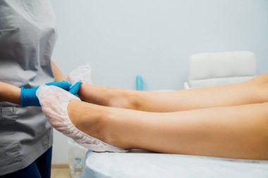 Mavi eldivenli kadın elleri müşterinin ayaklarına tek kullanımlık çoraplar giydirdi. Güzellik salonu ya da tıbbi prosedürler. Masaj veya pedikür.