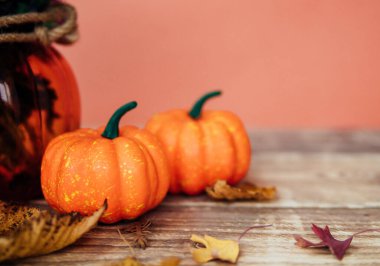 İki küçük dekoratif balkabağı ahşap bir masanın üzerinde yatıyor. Kuru sonbahar yaprakları etrafa saçıldı. Cadılar Bayramı için hazırlık.