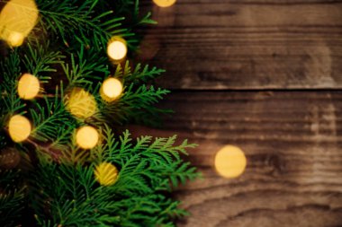 Yeşil thuja dallarının Noel ışıklarının arka planı. Ahşap tahtaların kahverengi yüzeyinde şenlikli parlak bir çelenk dallarla sarmalanmıştır. Noel ağacı süslemeleri konsepti.