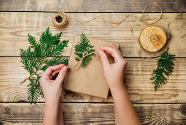 Kadınların elleri, tahta bir arka planda koli kâğıdına kutu doldurur. Teslimat servisi. Çevre dostu malzeme. El yapımı sanat eseri. Noel ve Yeni Yıl kavramı.