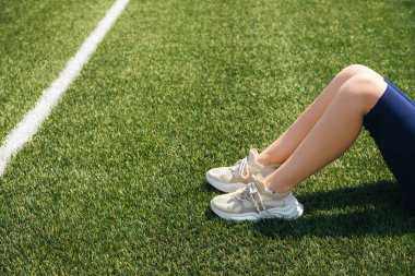 Yeşil yapay çimlerin üzerinde beyaz spor ayakkabılı bir kızın bacakları. Spor ayakkabılar. Aktif bir yaşam tarzı. Dinlenme ve rahatlama.