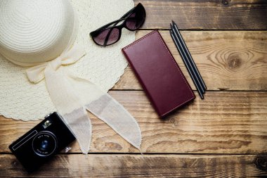 Yazlık hasır şapka, güneş gözlüğü, kamera, tahta bir arka planda defter. Yaz tatili, seyahat, turizm. Üst görünüm, metin için boşluk.