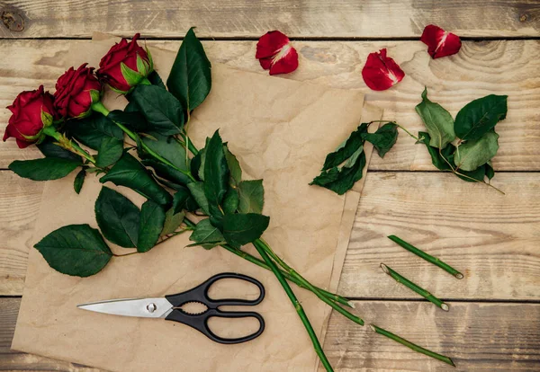 Çiçekçi, çiçekli bir gül aranjmanı oluşturur ve sapını makasla budarlar. Bitkileri tazeler. Şenlik havası.