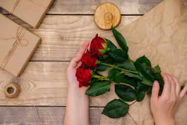 Üst manzara, kadın elleri ahşap arka planda bir buket kırmızı gül tutuyor. Neşeli bir atmosfer. Bir tebrik kartı ya da davetiye.