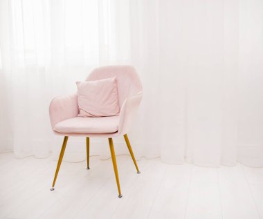 Açık pembe bir koltuk beyaz havadar perdelerin arka planına karşı pencerenin yanında durur. Modern iç tasarımı çok şık. Odada yalnız bir sandalye.