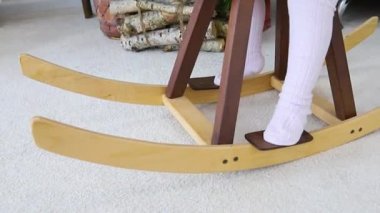 A little girl is swinging on a wooden toy horse. Close-up of the baby's legs. Children's toy made of natural wood. A fun game.