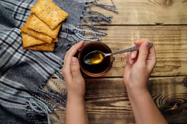 Kadınların elleri bir fincan koyu kahveyi ahşap bir arka planda tutar. Lezzetli kurabiyeler, sıcak bir eşarp, yazı için bir yer..