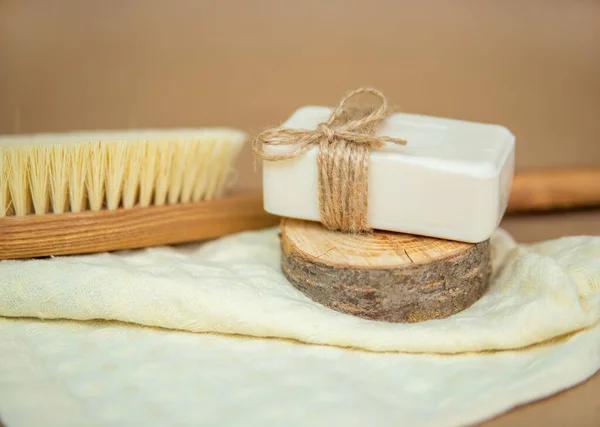 A wooden brush for dry body massage and natural soap lie on a towel. Foot brush and pumice stone for heels on beige background. Environmentally friendly material. Accessories for skin care.