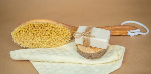 A wooden brush for dry body massage and natural soap lie on a towel. Foot brush and pumice stone for heels on beige background. Environmentally friendly material. Accessories for skin care.